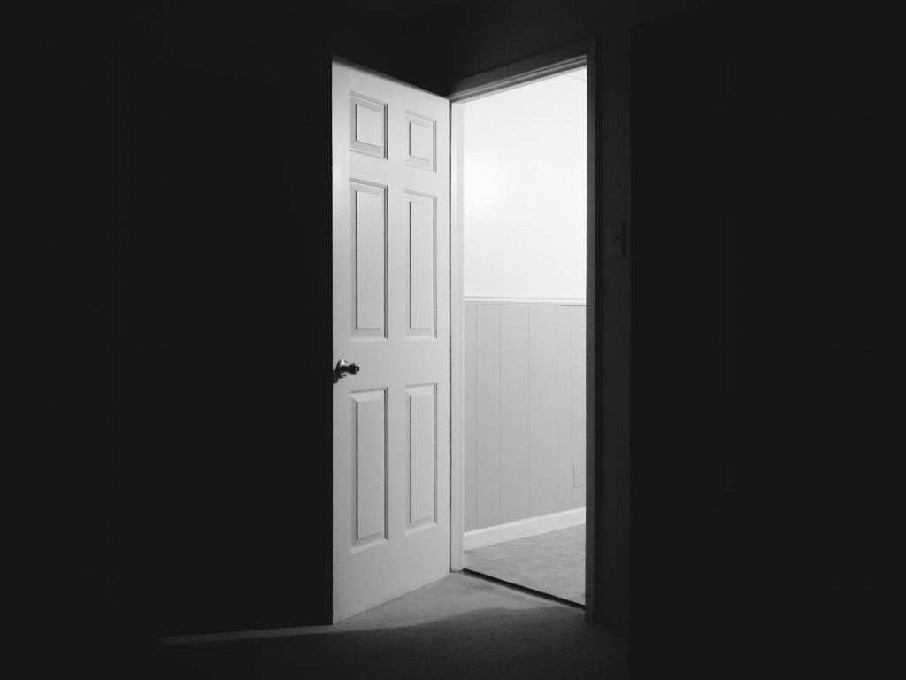 An open door in a hallway at night. 